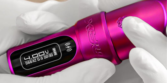 Gloved hands holding a vibrant pink cordless tattoo machine displaying its digital voltage screen.