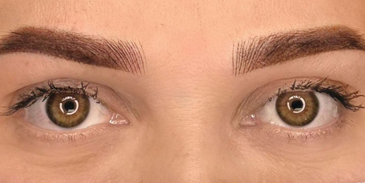 Symmetrical tattooed eyebrows above both brown eyes.