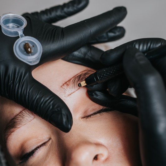 A permanent makeup artist using a microblading tool to tattoo hair-like strokes on a client's eyebrow.